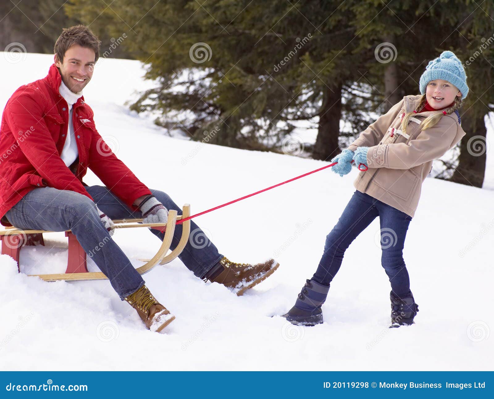 Young Girl Pulling Father Through Snow On Sled smiling at camera