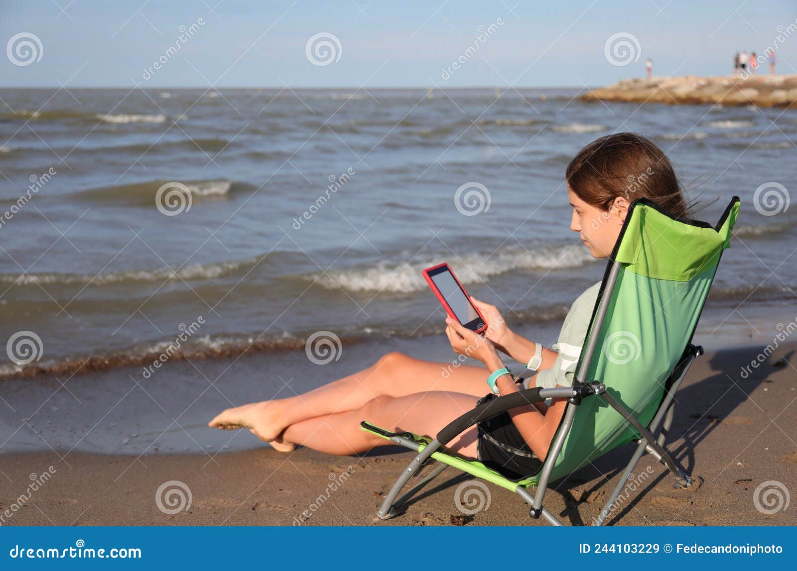 young girl reads an ebook on the deckchair relaxing by the sea