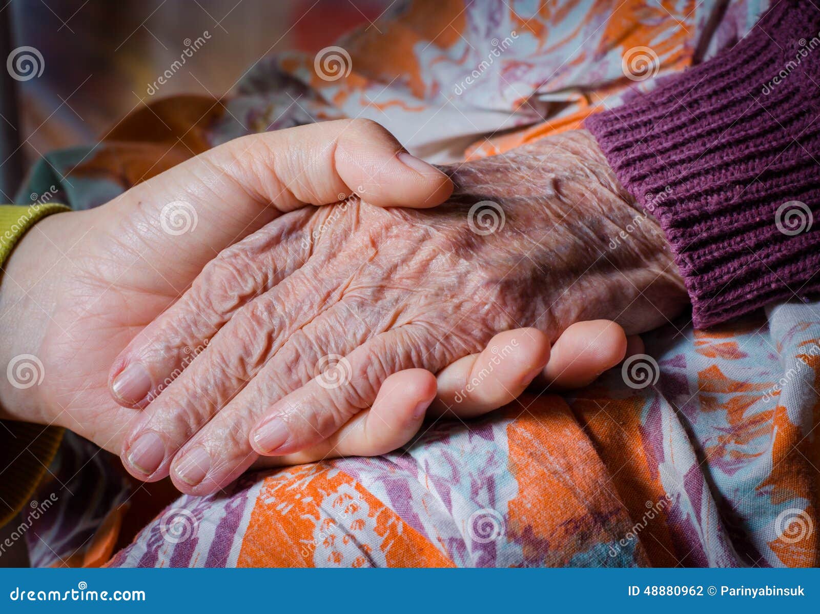young girl's hand touches and holds an old woman hand