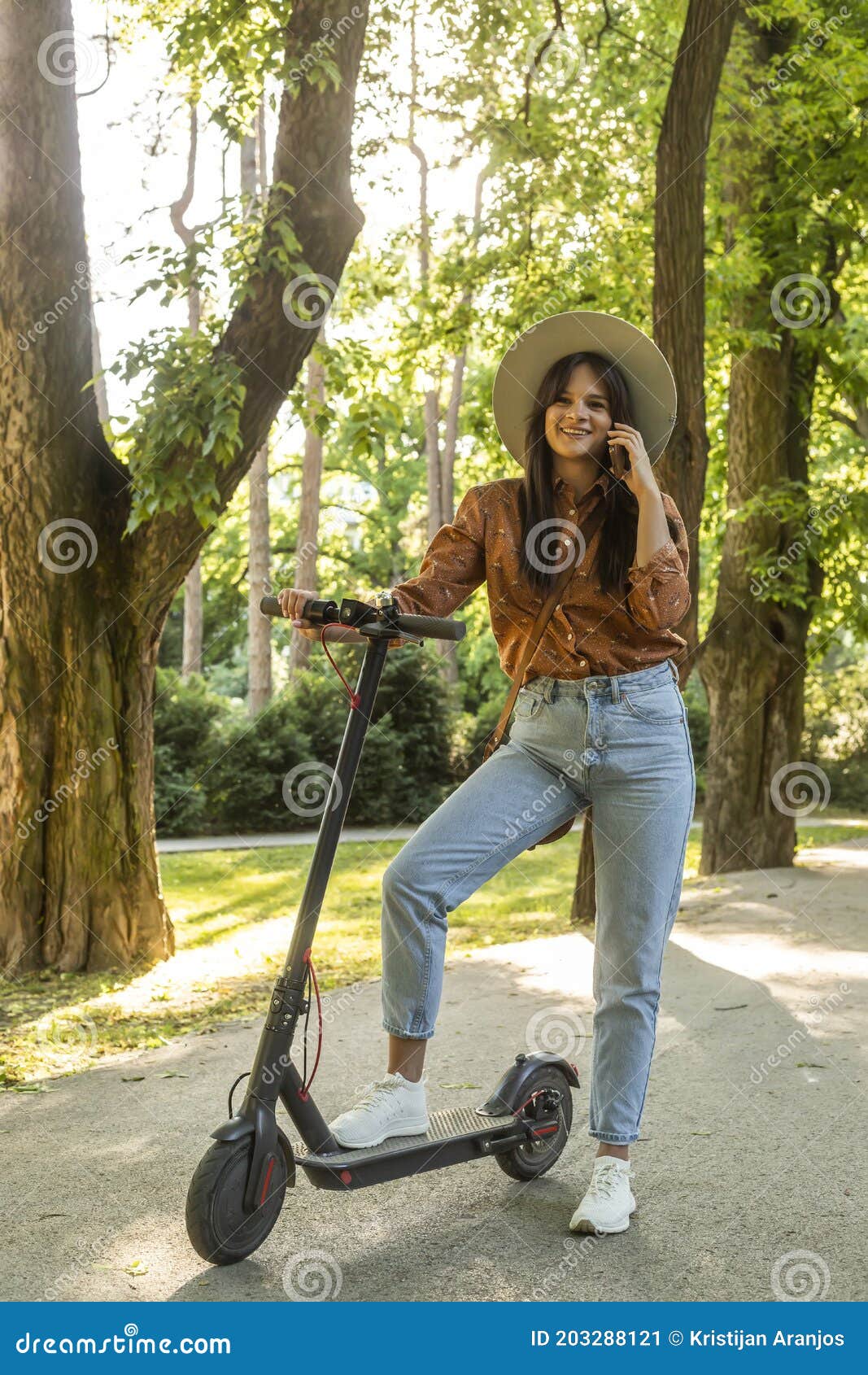 A Young Woman is Standing with Her Electric Scooter in the Park while ...