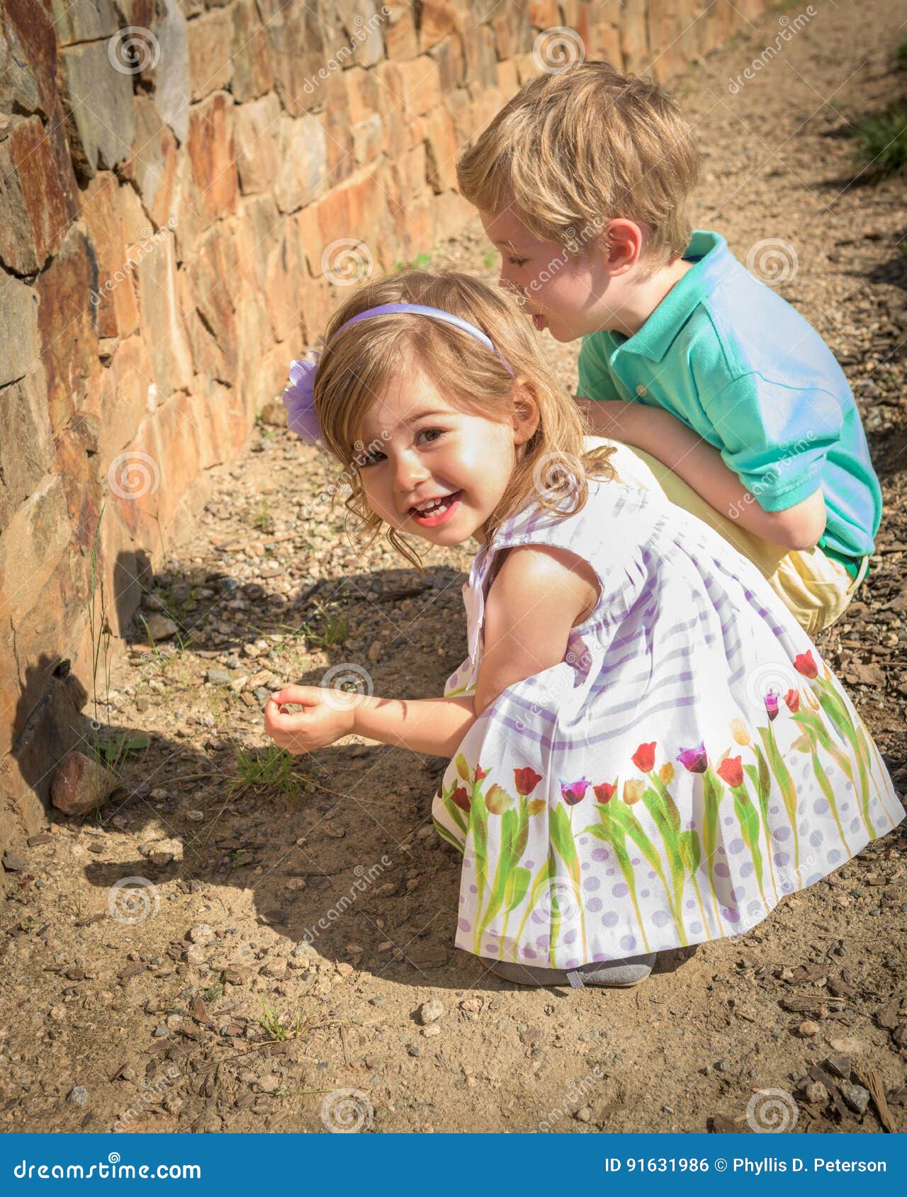 a young girl of 3 years and a boy of 5 years rest in a rock garden.