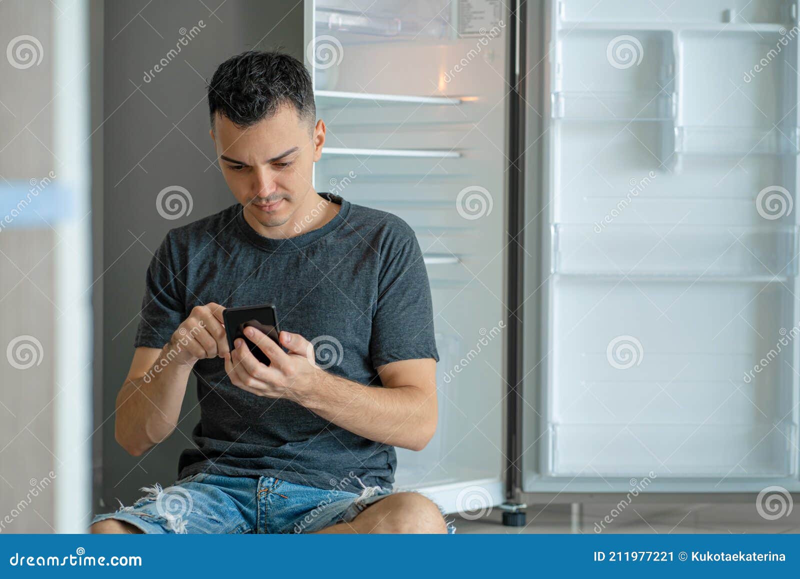A Young Guy Orders Food Using a Smartphone. Empty Refrigerator with No