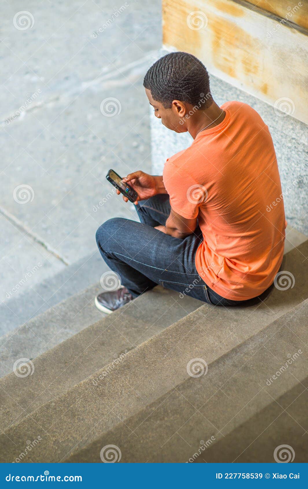 Young Black Man Sitting on Stairs Inside Office Building, Texting on