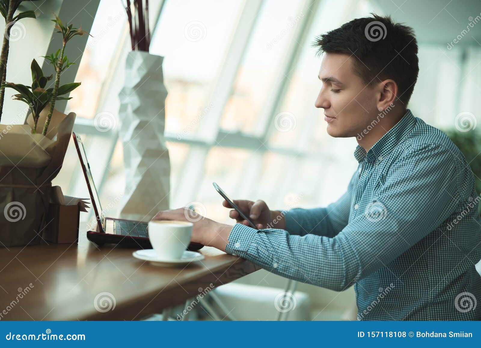 young handsome businessman checks his smartphone while working in cafe with a cup of americano