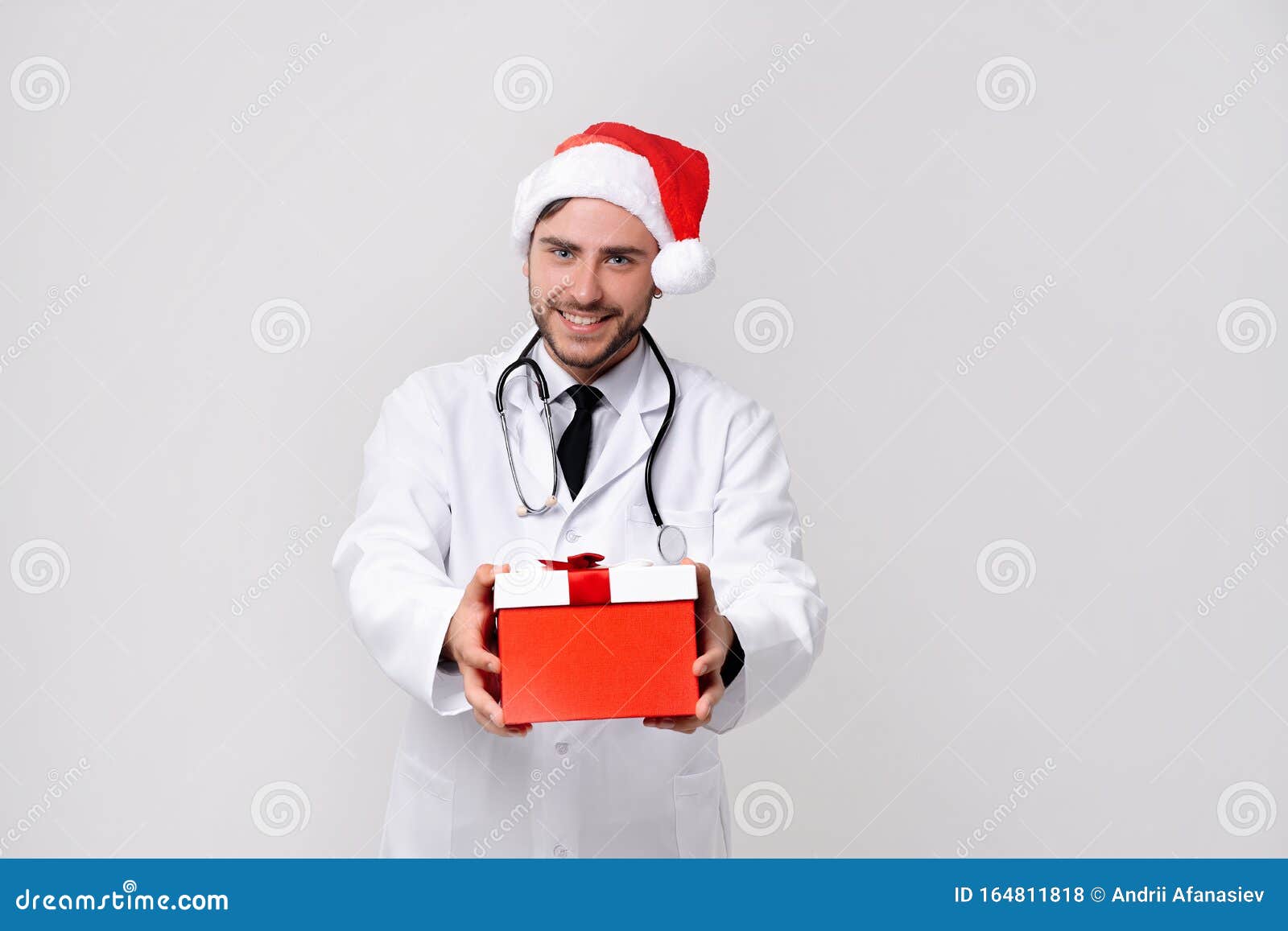 young handsome doctor in white uniforme and santa claus hat standing in studio on white background smile and finger in camera