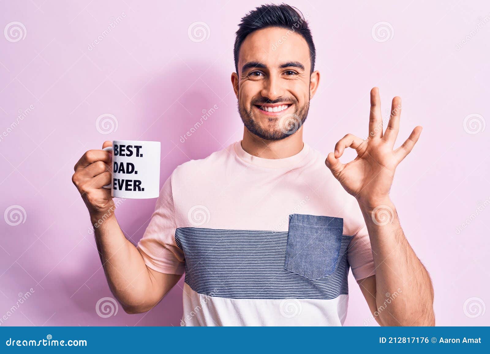 young handsome man with beard drinking mug of coffee with best dad ever message doing ok sign with fingers, smiling friendly