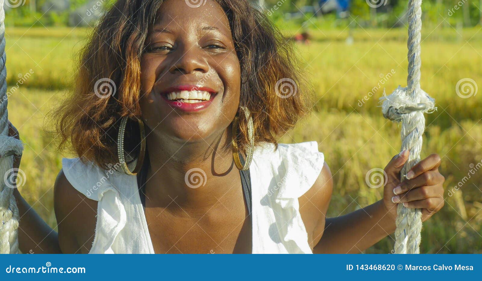 young happy and beautiful black african american woman in summer dress playing outdoors on swing smiling cheerful and relaxed