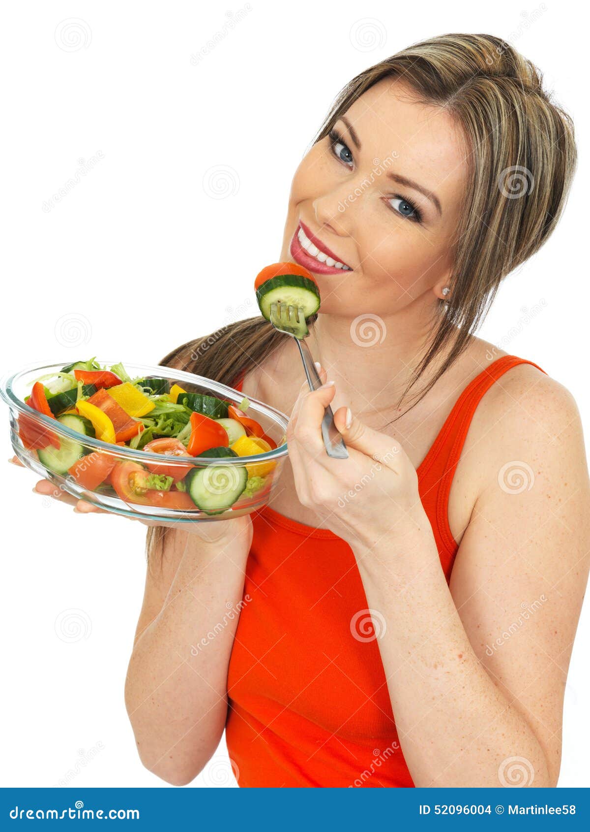 Young Happy healthy Woman Eating a Fresh Mixed Garden Salad. A DSLR royalty free image, a young healthy happy attractive woman, holding and eating a freshly mixed garden salad, smiling towards the camera, wearing a red or orange vest top, shot against a white background.