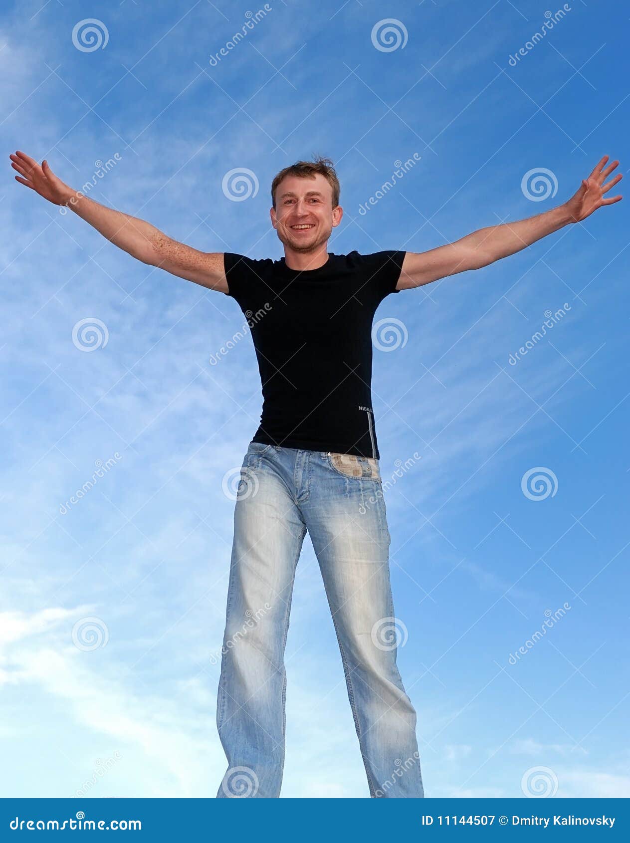 Young happy man with open arms outdoors over blue sky