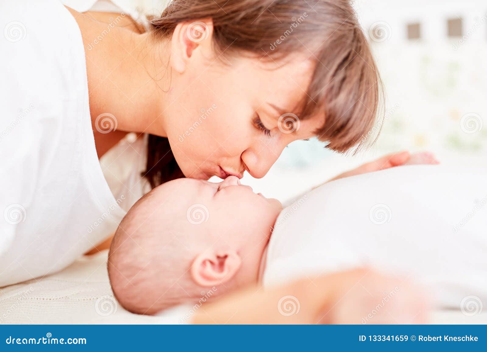 Мама дают сину. Мама целует грудничка. Поцелуй молоденцев. Взрослая женщина целует новорожденного дома. Взрослая женщина целует новорожденного горизонтальное.