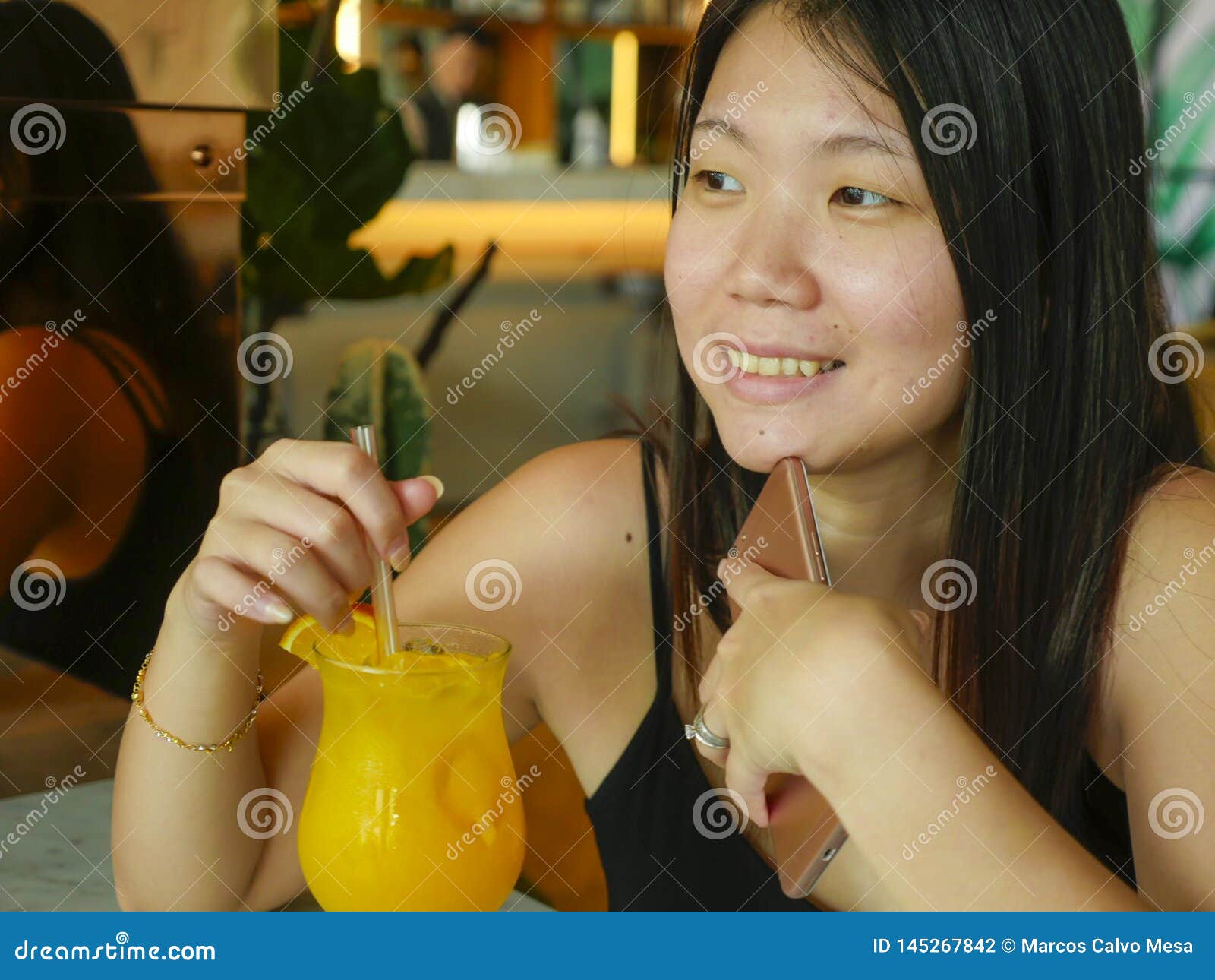 young happy and relaxed asian chinese tourist woman drinking healthy orance juice at hotel cafe or restaurant resort smiling
