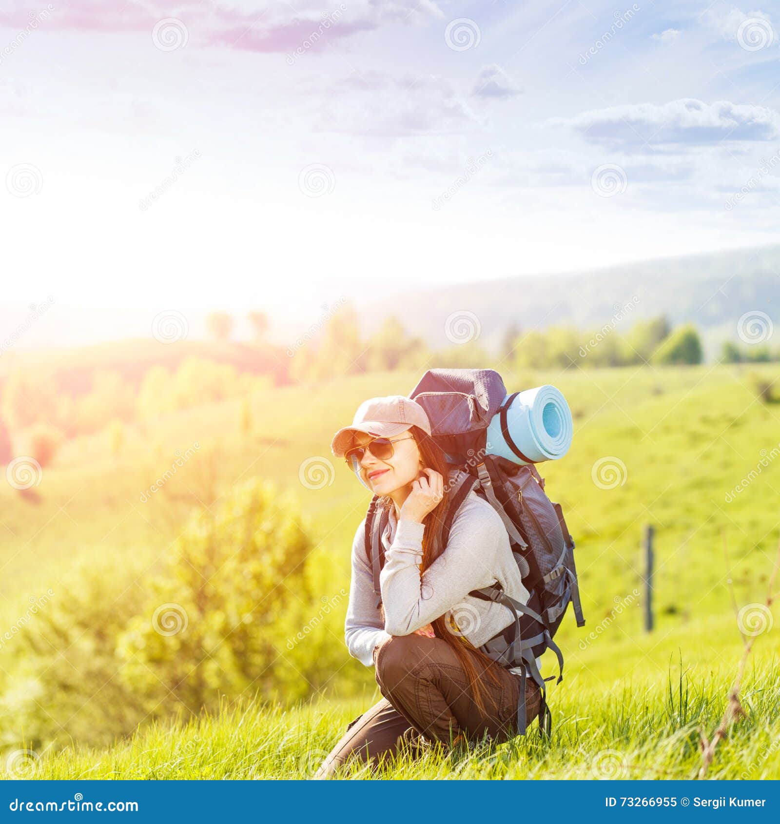 Young happy woman with backpack resting on hill. Young happy woman with backpack resting on green hill in sunrise beams. Beautiful traveling backpacker background with copy space