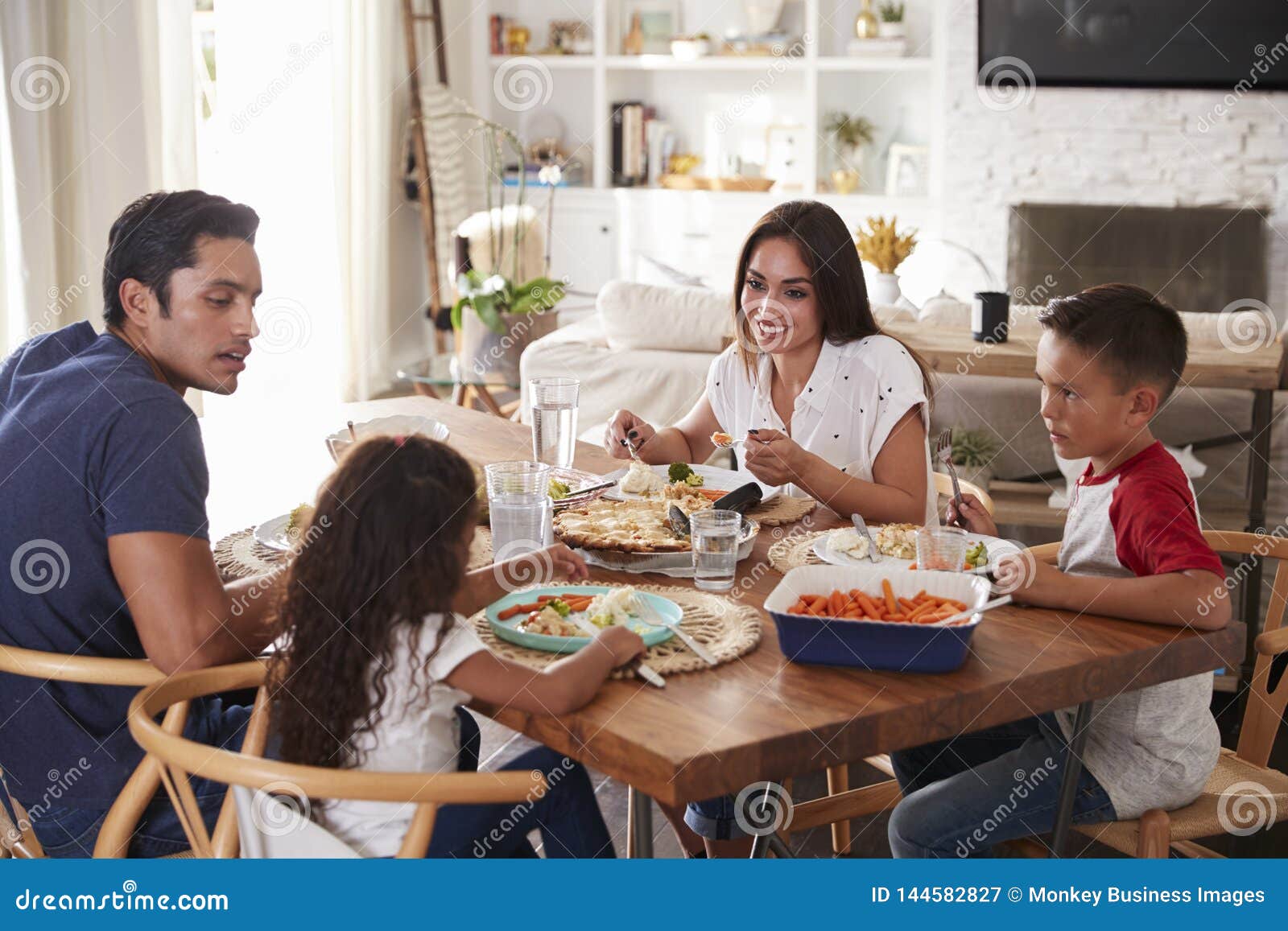 young hispanic family sitting at dining table eating dinner together