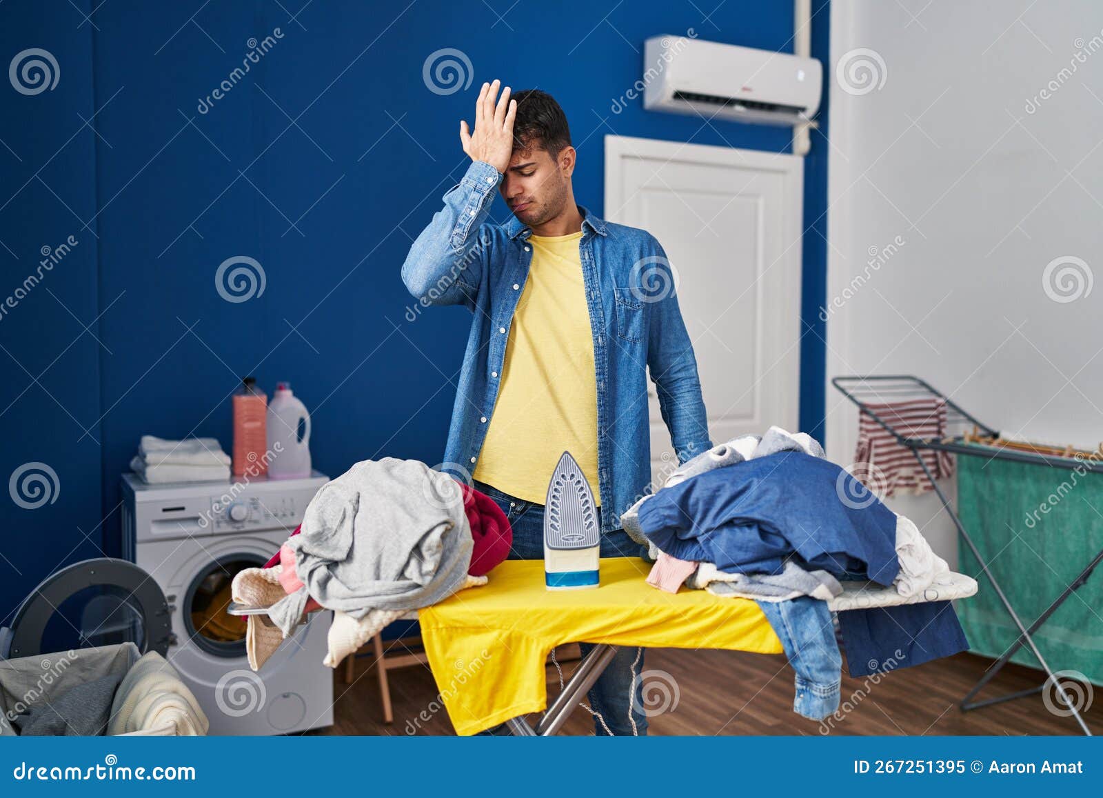 Young Hispanic Man Ironing Clothes at Home Surprised with Hand on Head