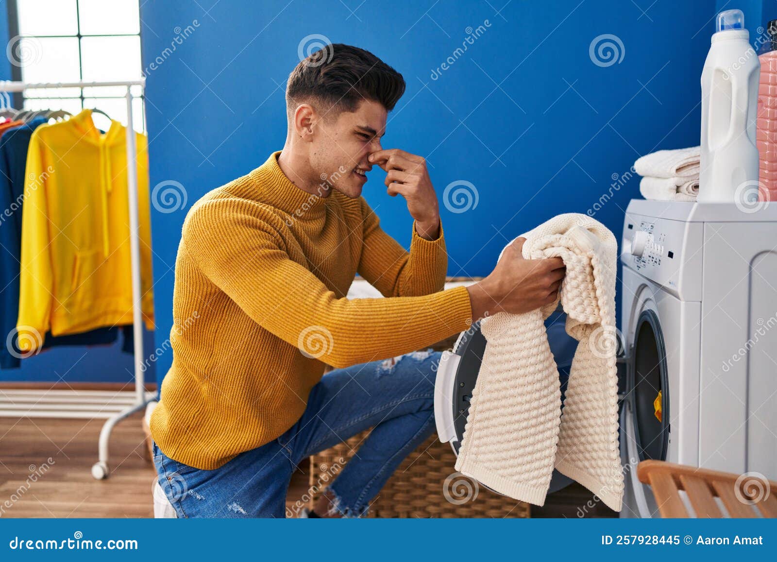 Young Hispanic Man Washing Clothes Smelling Dirty Clothes at Laundry