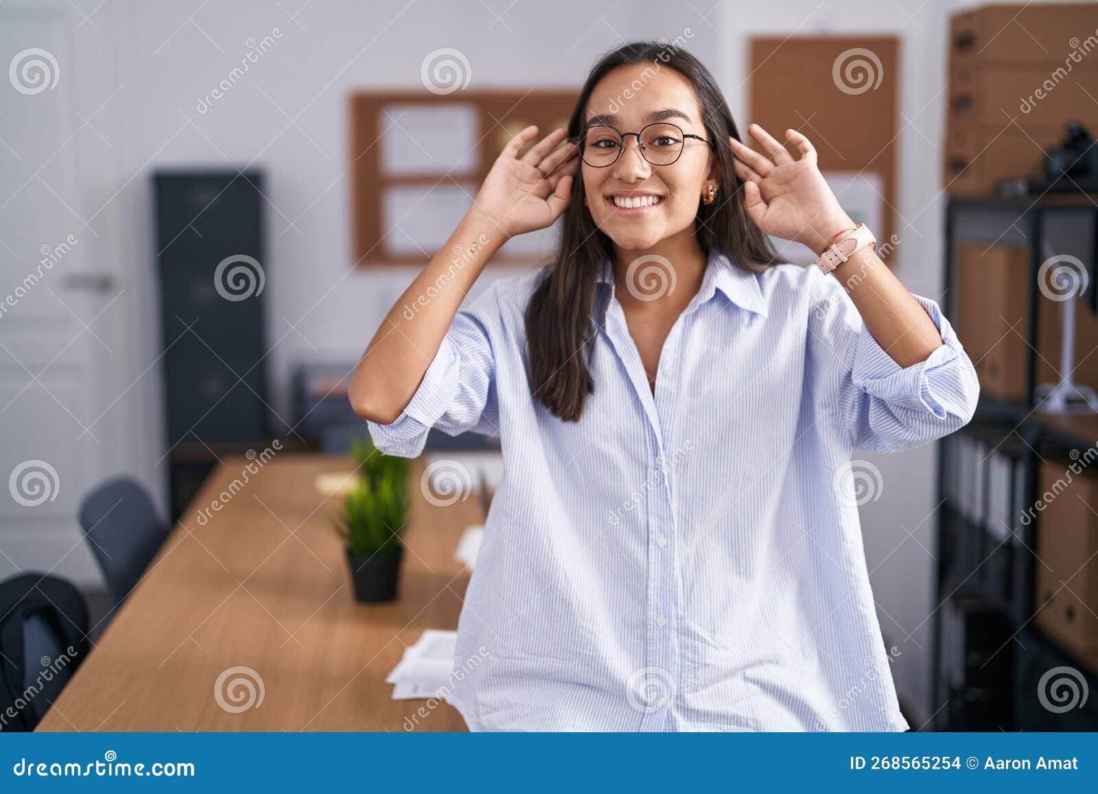 Young Hispanic Woman at the Office Smiling Pulling Ears with Fingers