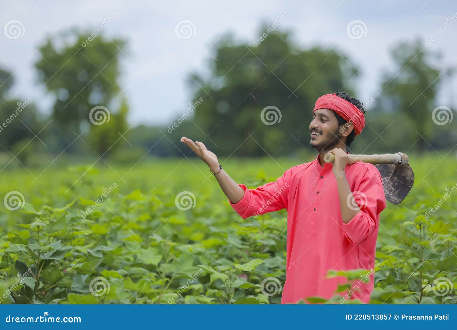 young indian farmer holding farm equipment in hand at cotton field