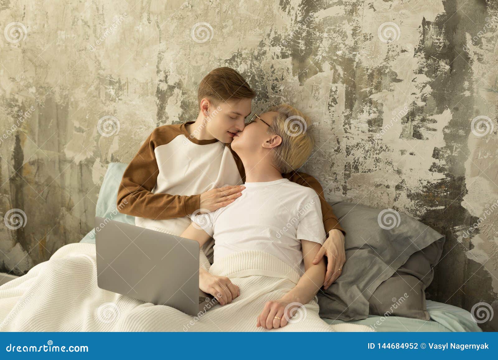 Young International Same Sex Male Couple Spending Time Together in One Bed Watching Laptop Stock Photo pic
