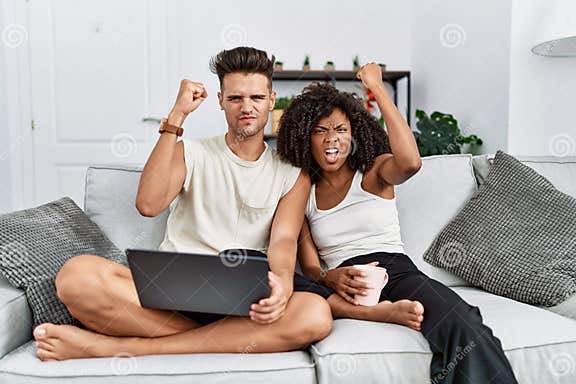 Young Interracial Couple Using Laptop At Home Sitting On The Sofa Angry