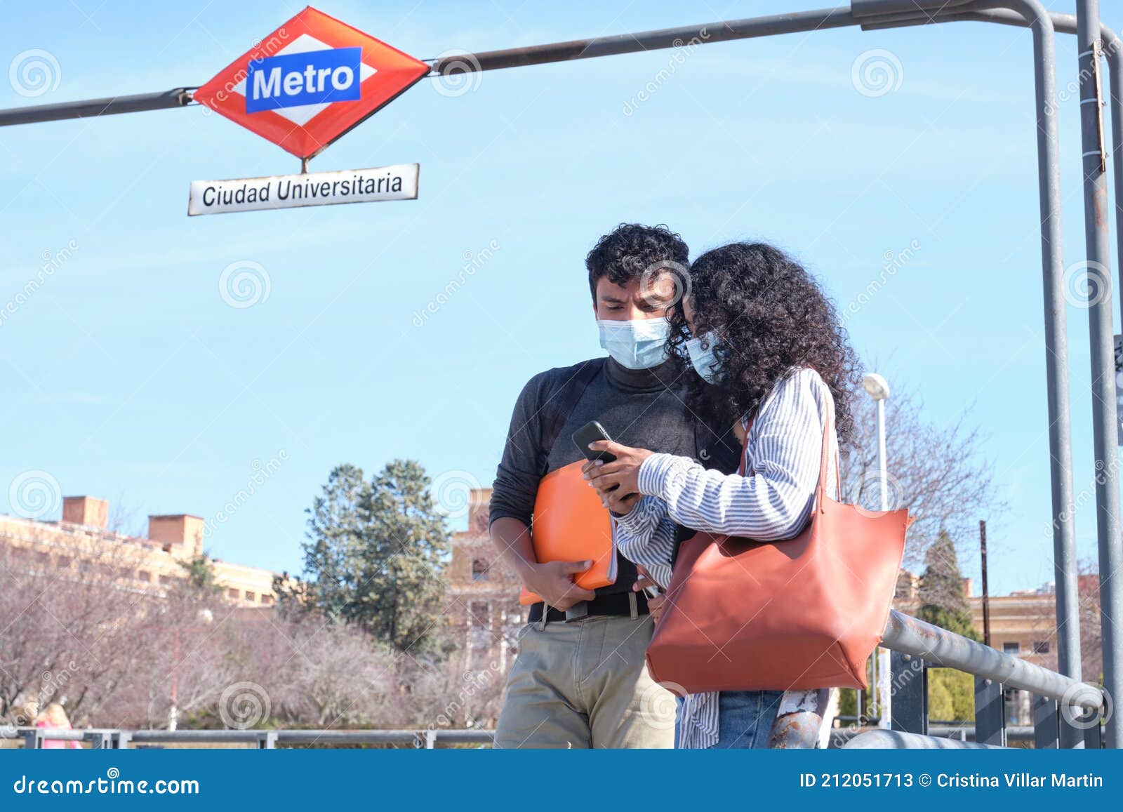 young latin couple wearing protective face mask looking at the smartphone at ciudad universitaria train stop