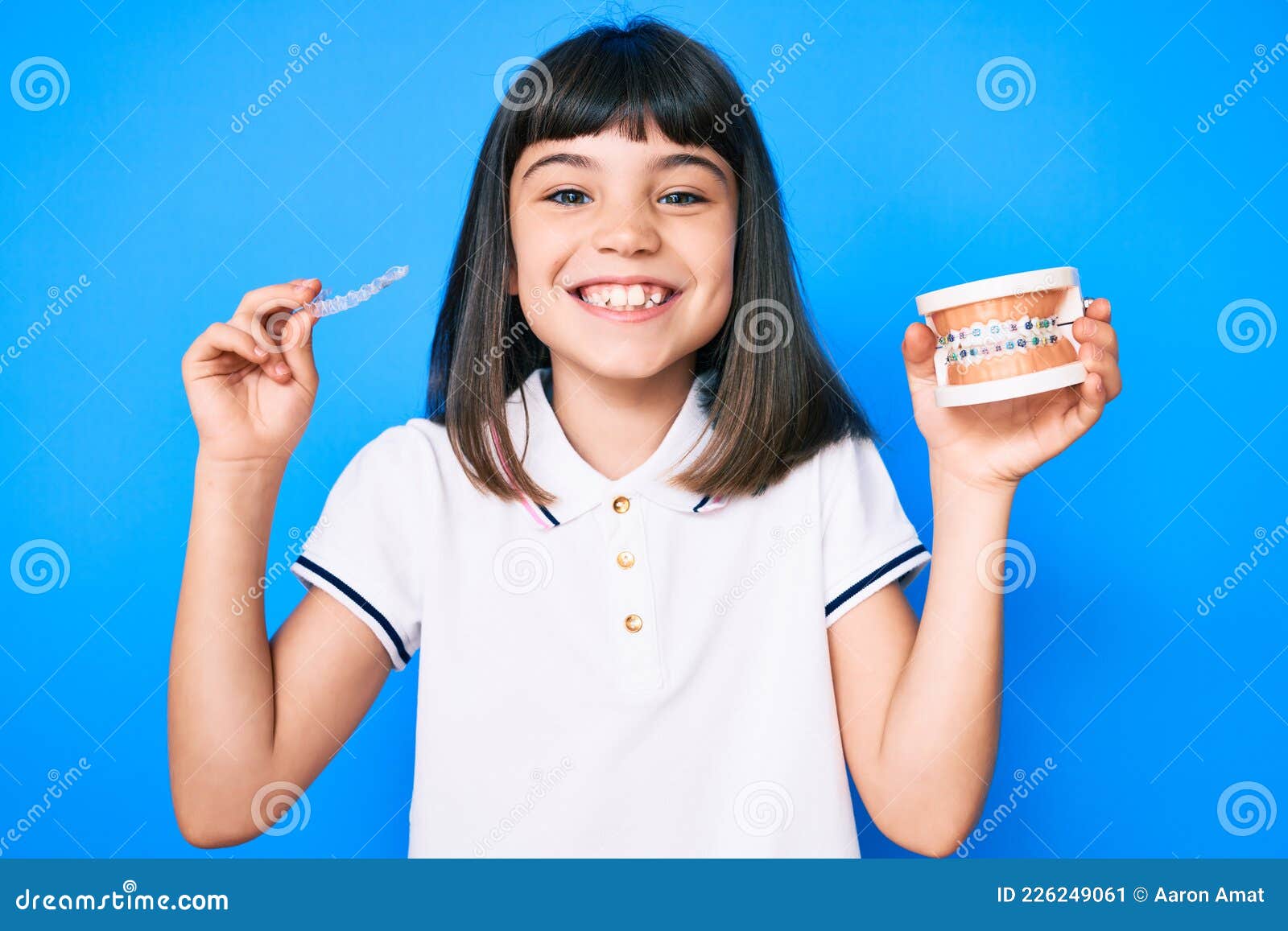 young little girl with bang holding invisible aligner orthodontic and braces smiling with a happy and cool smile on face