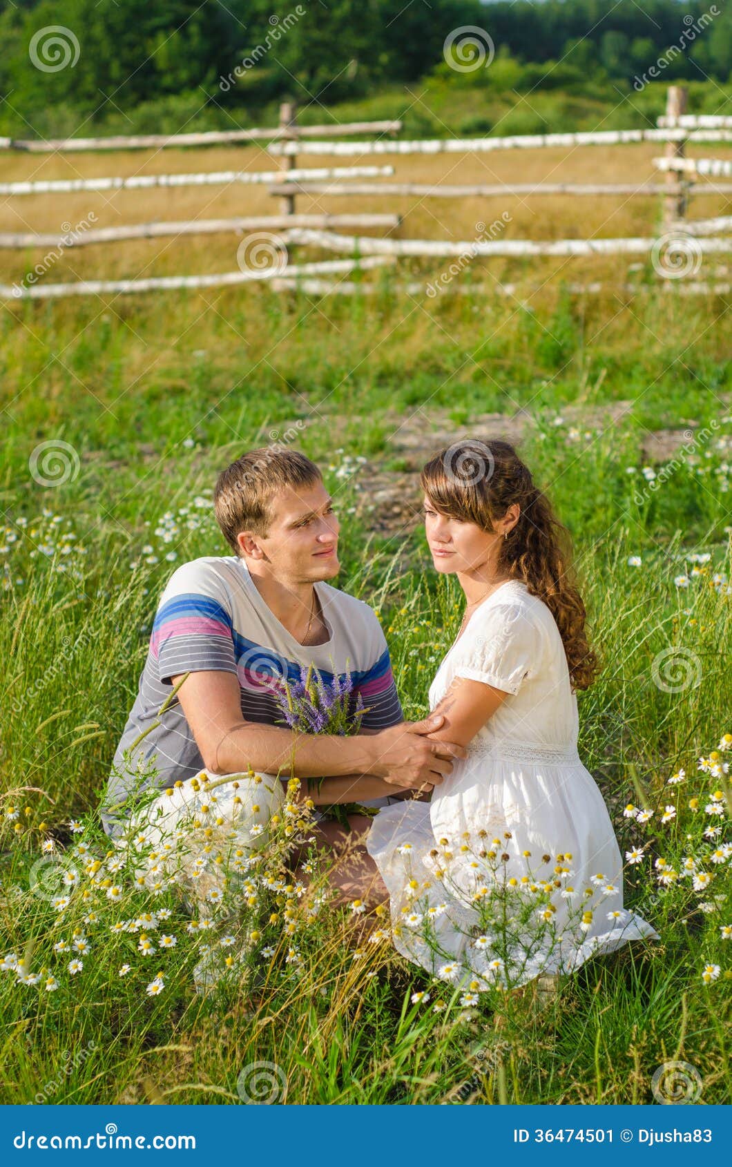 Young Loving Couple Embracing Each Other Sitting in the Grass Stock