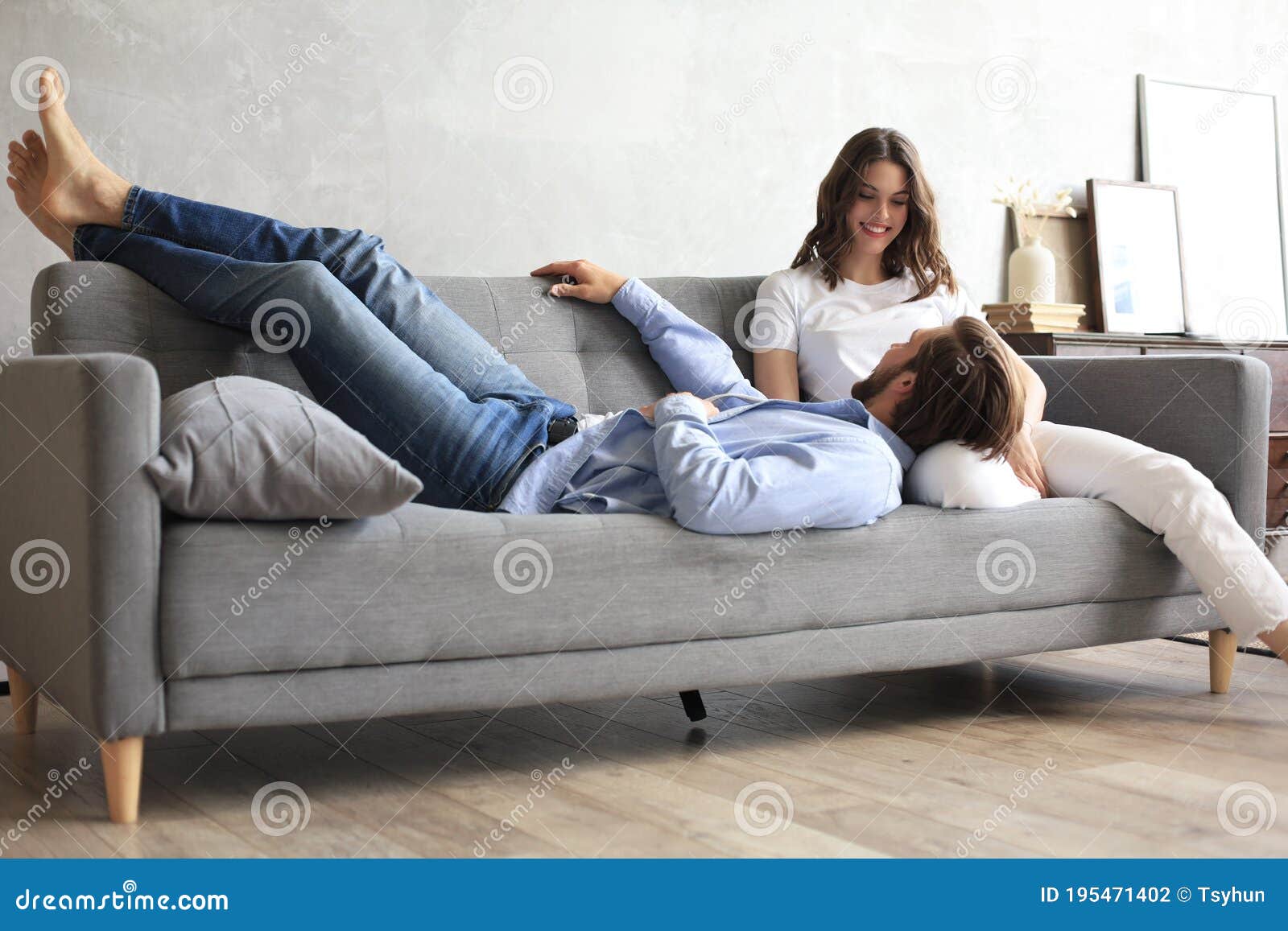 young loving couple relaxing on sofa together, husband lying on wife legs resting on couch