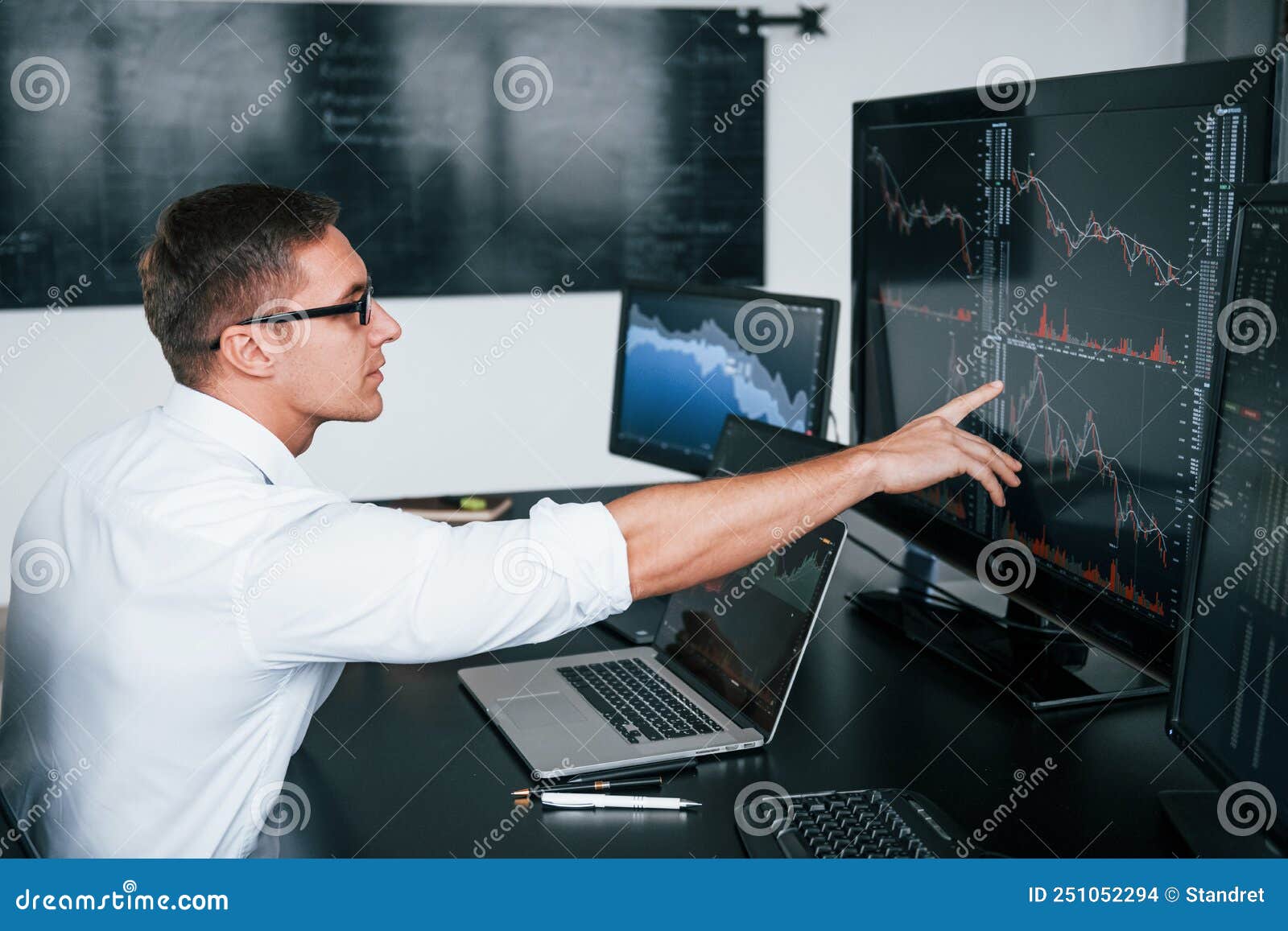 young male stock brocker works indoors in the office. many of displays