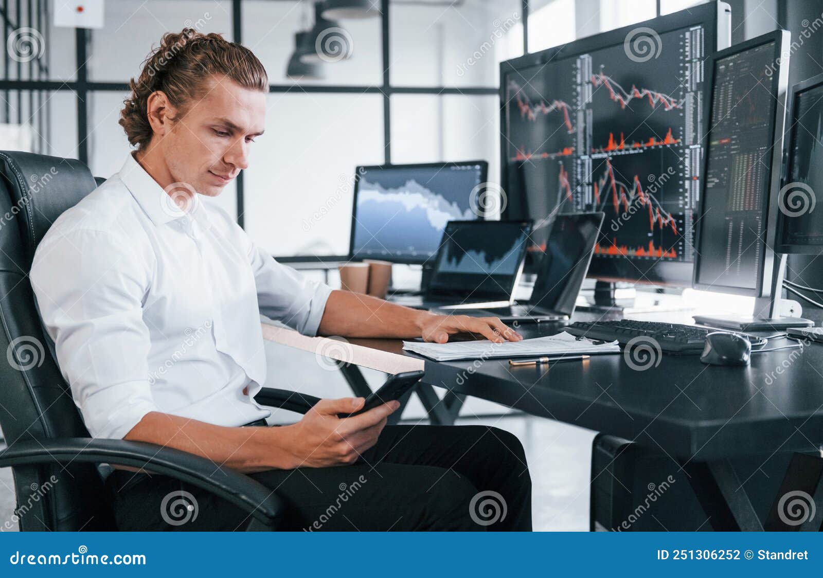 young male stock brocker works indoors in the office. many of displays