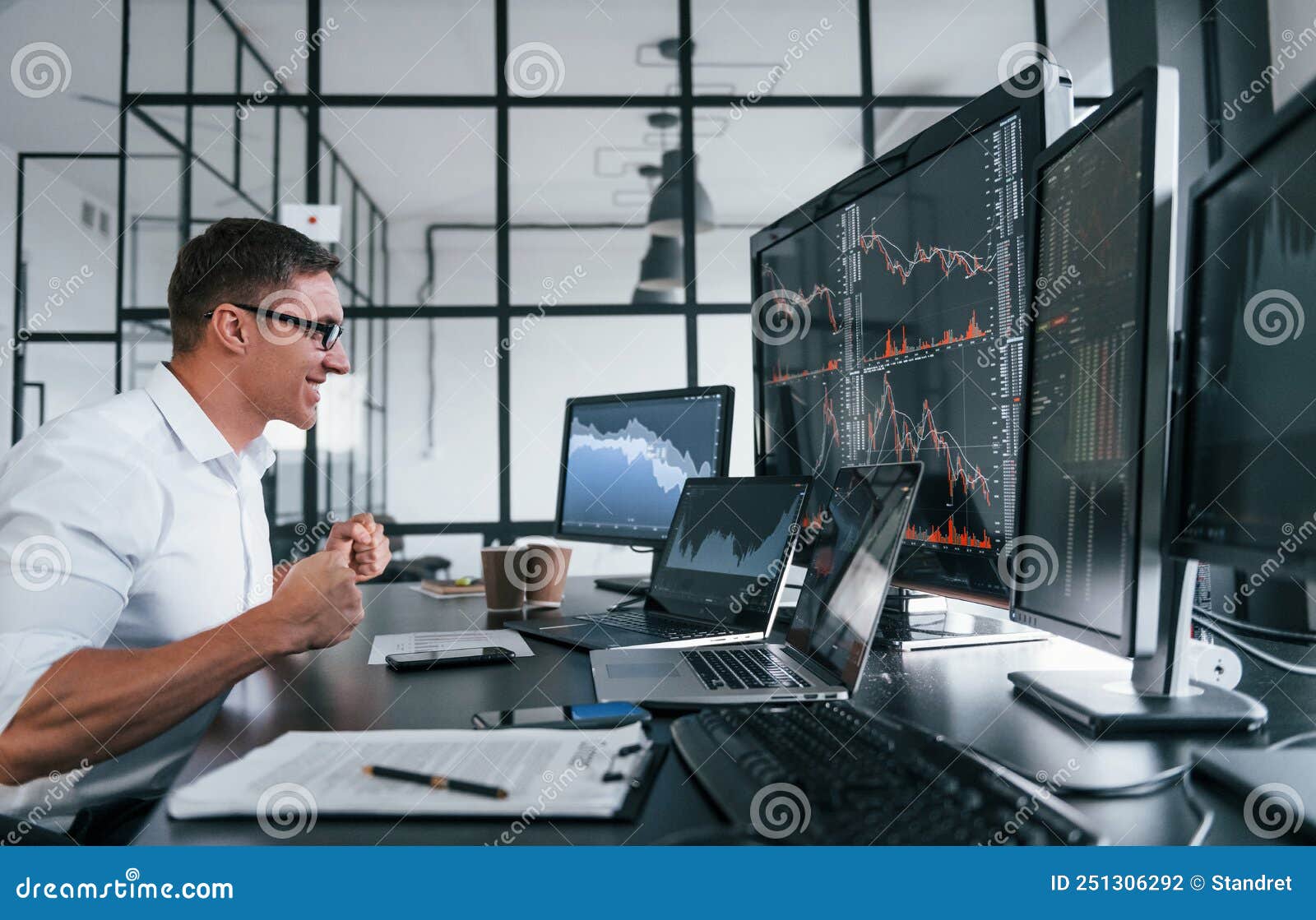 young male stock brocker works indoors in the office. many of displays