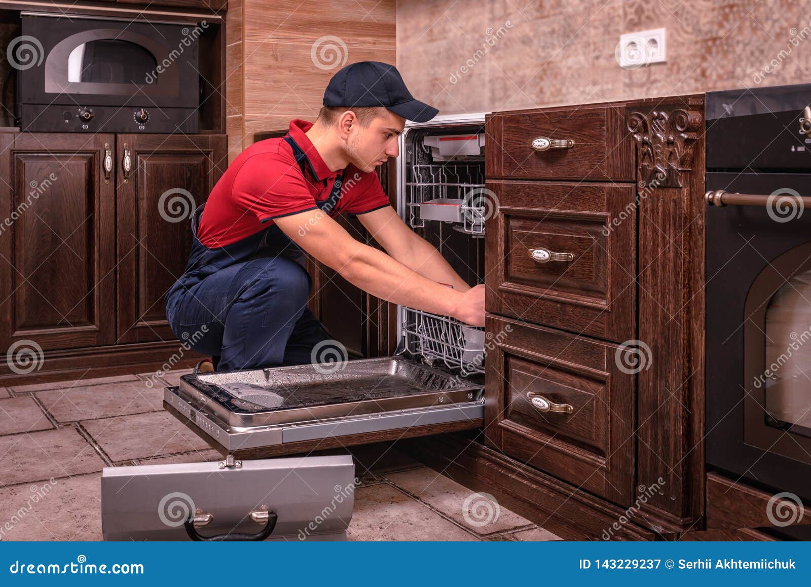 Young Male Technician Repairing Dishwasher in Kitchen Stock Image