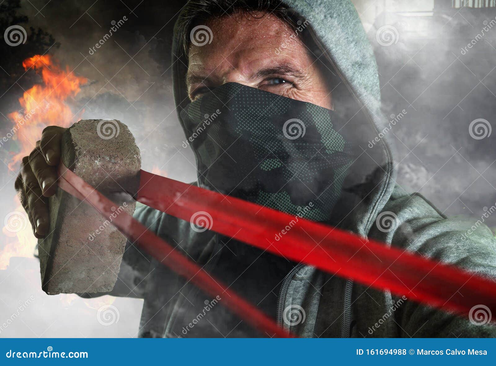 young man as ultra and radical anarchist rioter . furious antifa protester in face mask throwing brick hostile on street on