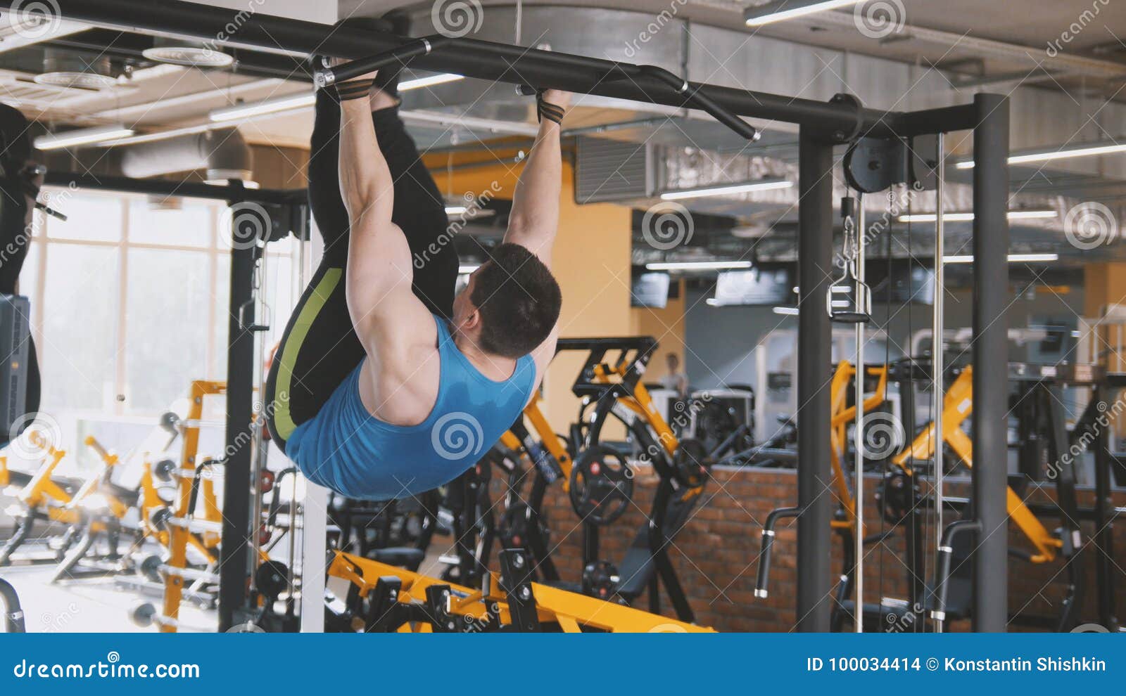 Young Man Athlete Doing Pullup Bar Abdominal Exercise in Gym Stock