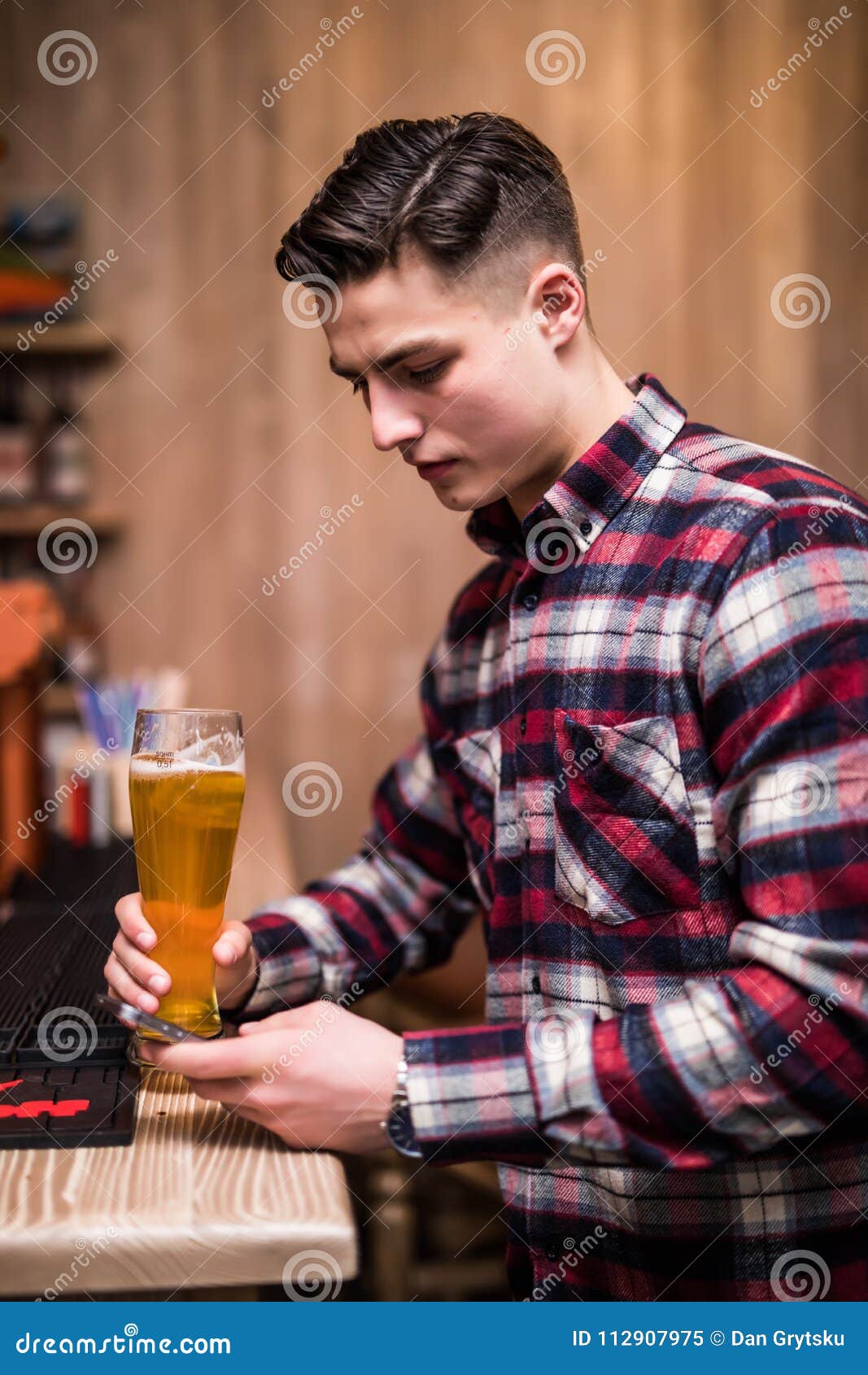 young man with beer bottle using phone at counter in pub