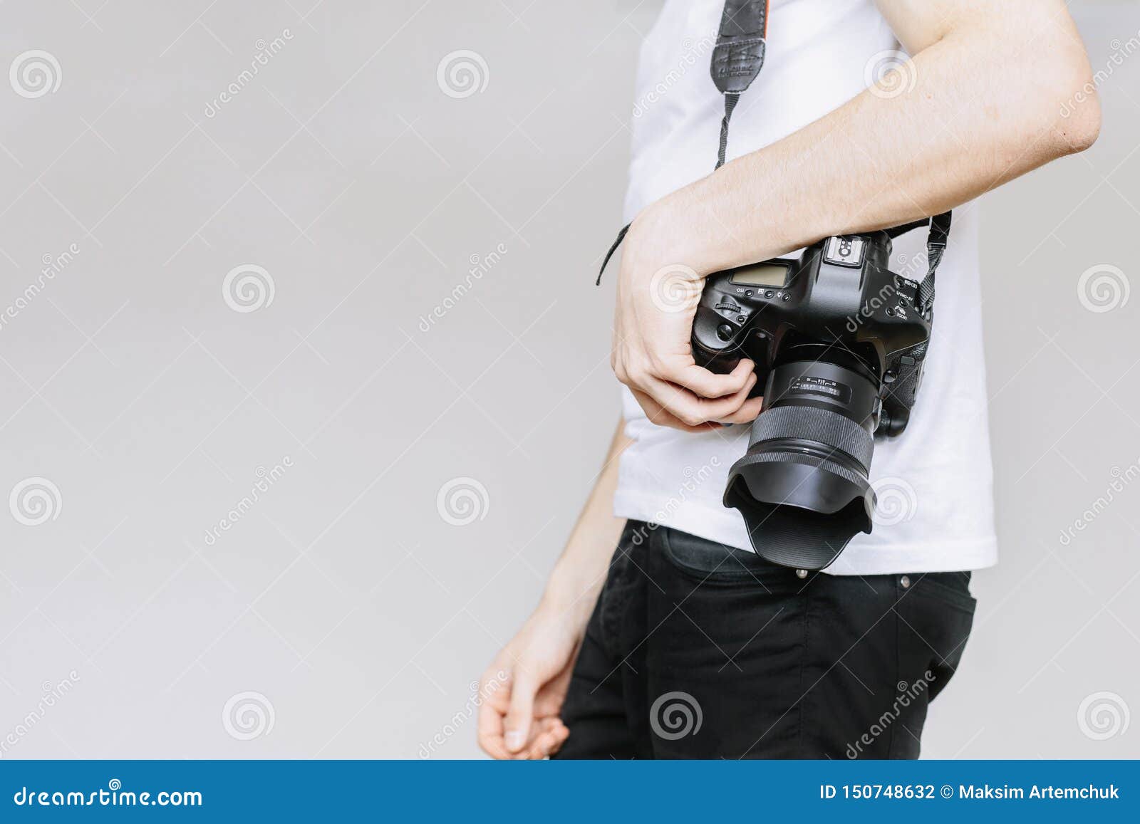 young man carries a photo camera on his shoulder.  gray background