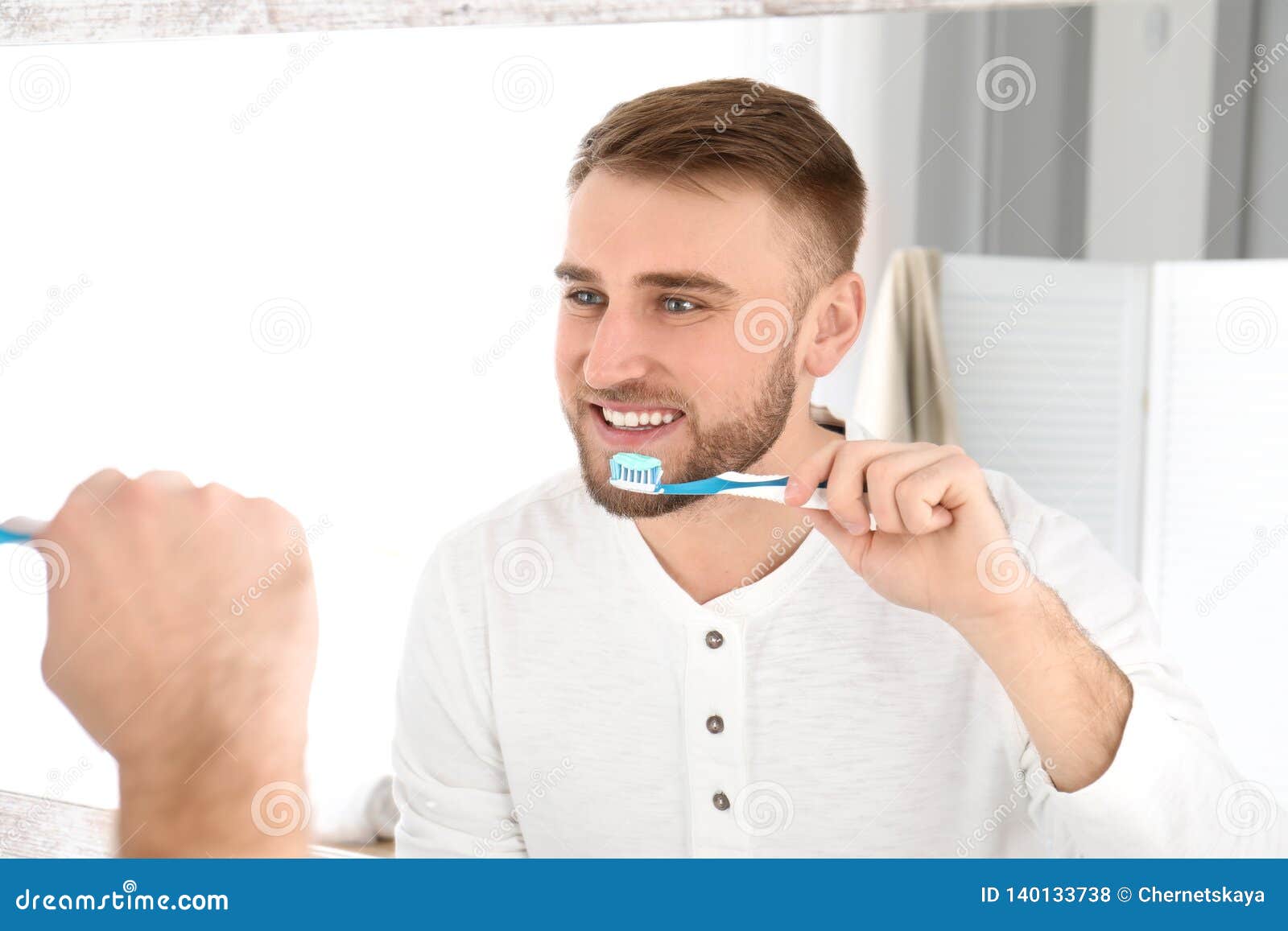 Young Man Cleaning Teeth Against Mirror Stock Photo