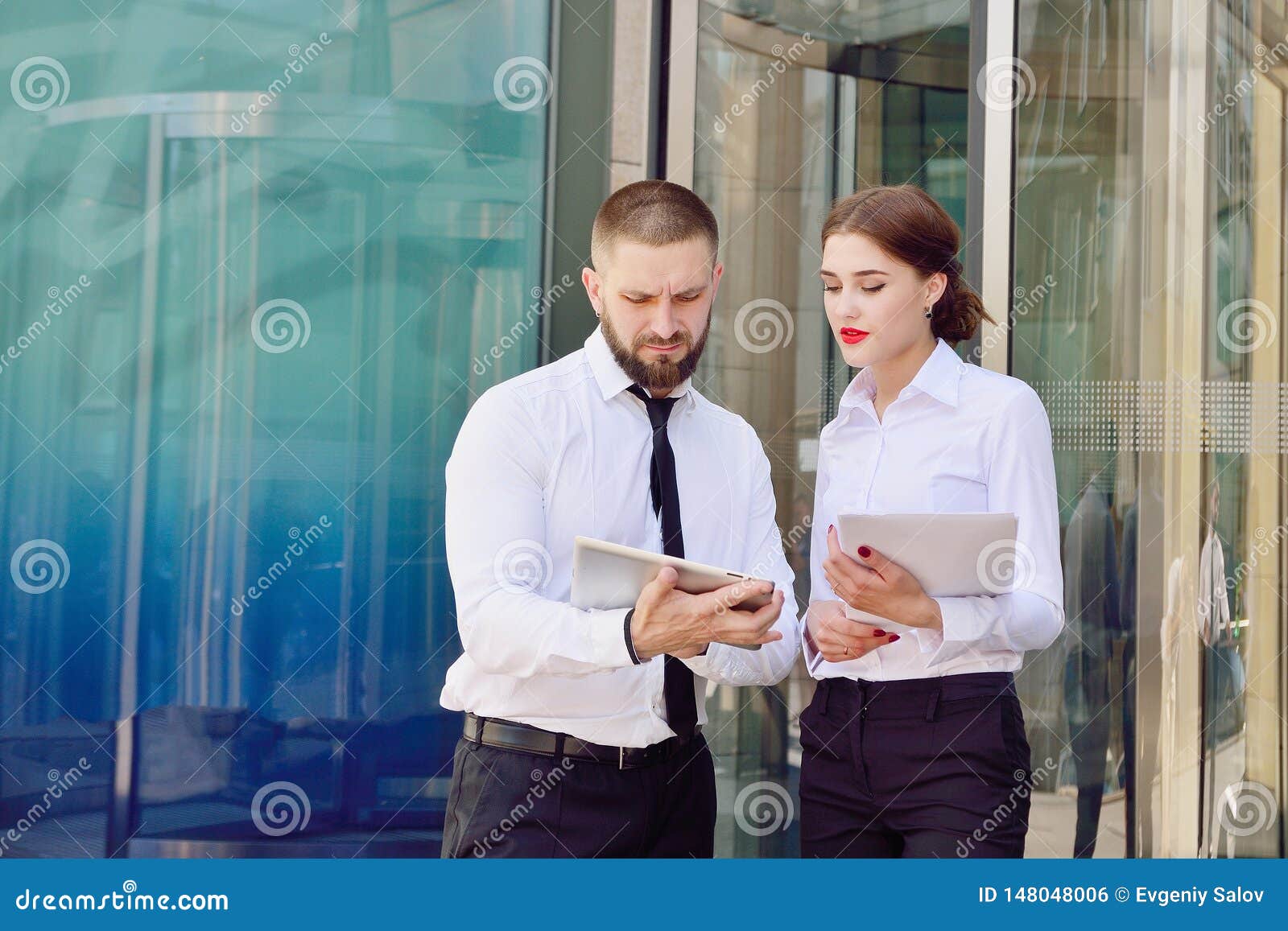 Young man and girl in white shirts with a tablet. Young men and girl in white shirts with a tablet on the background of an office building. Office workers