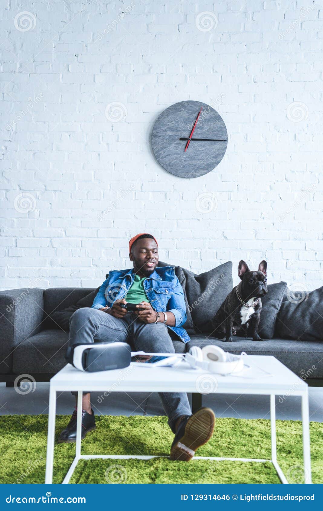 young man holding joystick while sitting on sofa with bulldog and digital gadgets