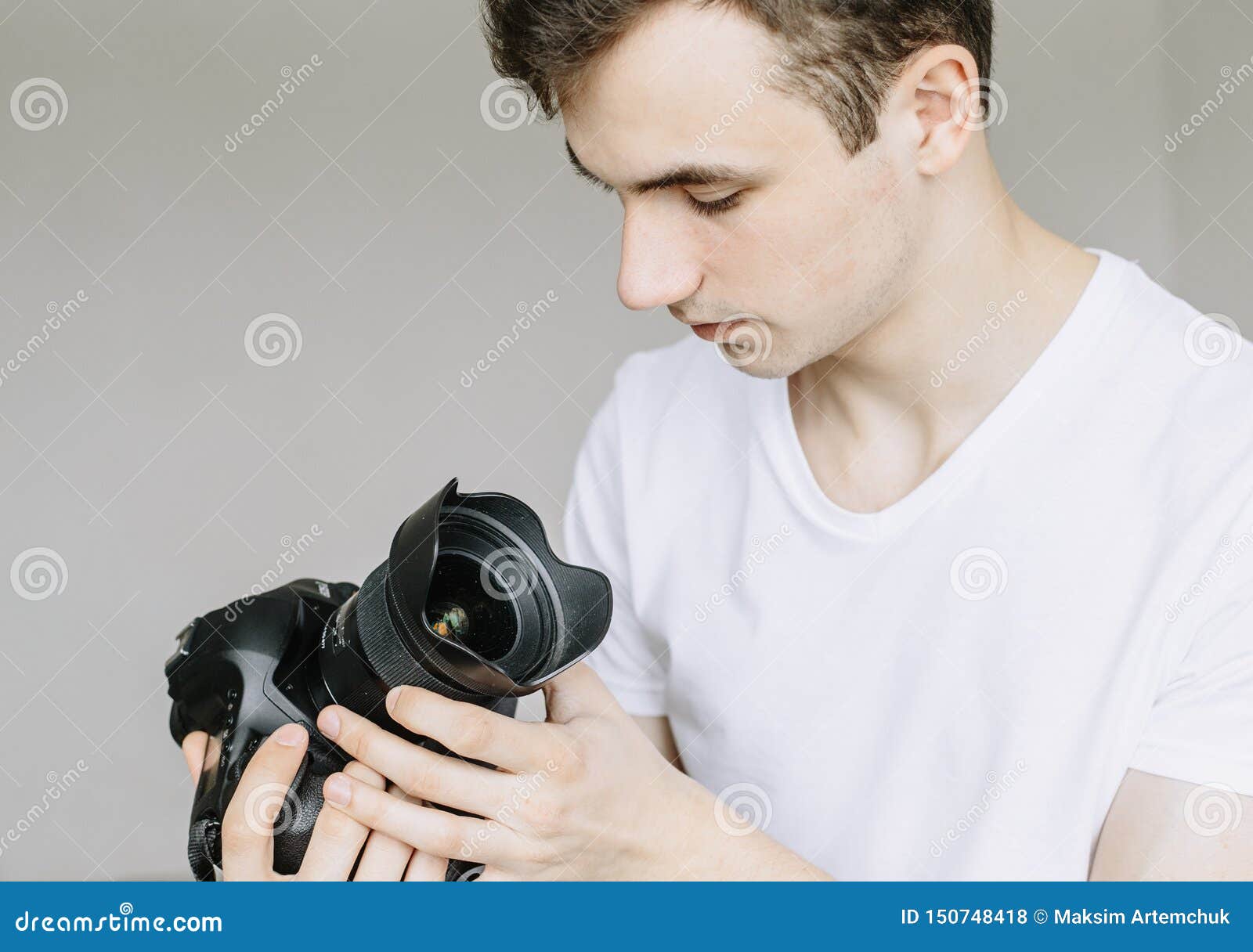 a young man holds a photo camera in his hand and looks at the lens in the dust, a dirty lens.  gray background