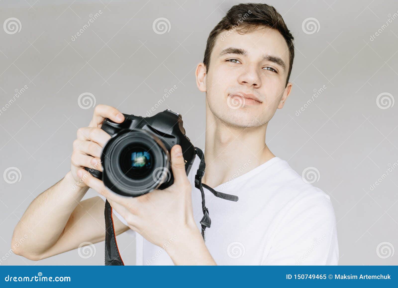 a young man holds a photo camera in his hand and looks straight.  gray background