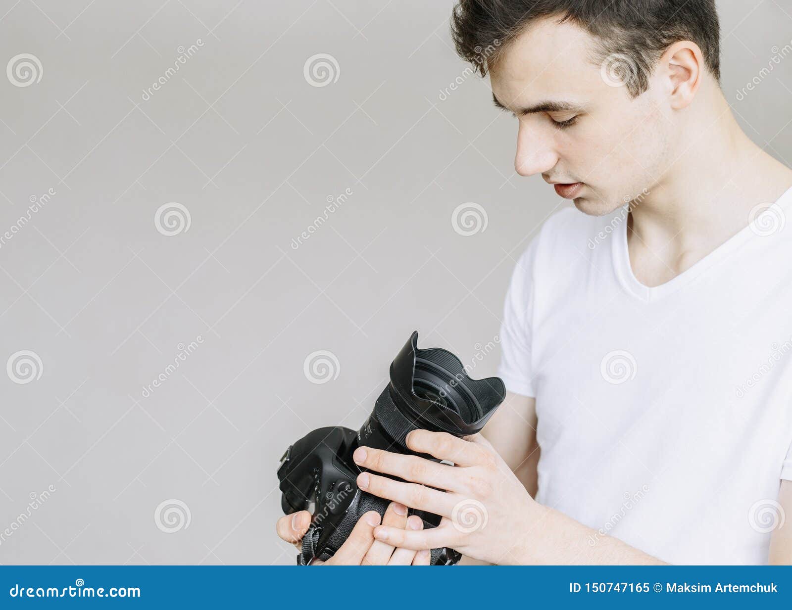 a young man holds a photo camera and looks at it.  gray background