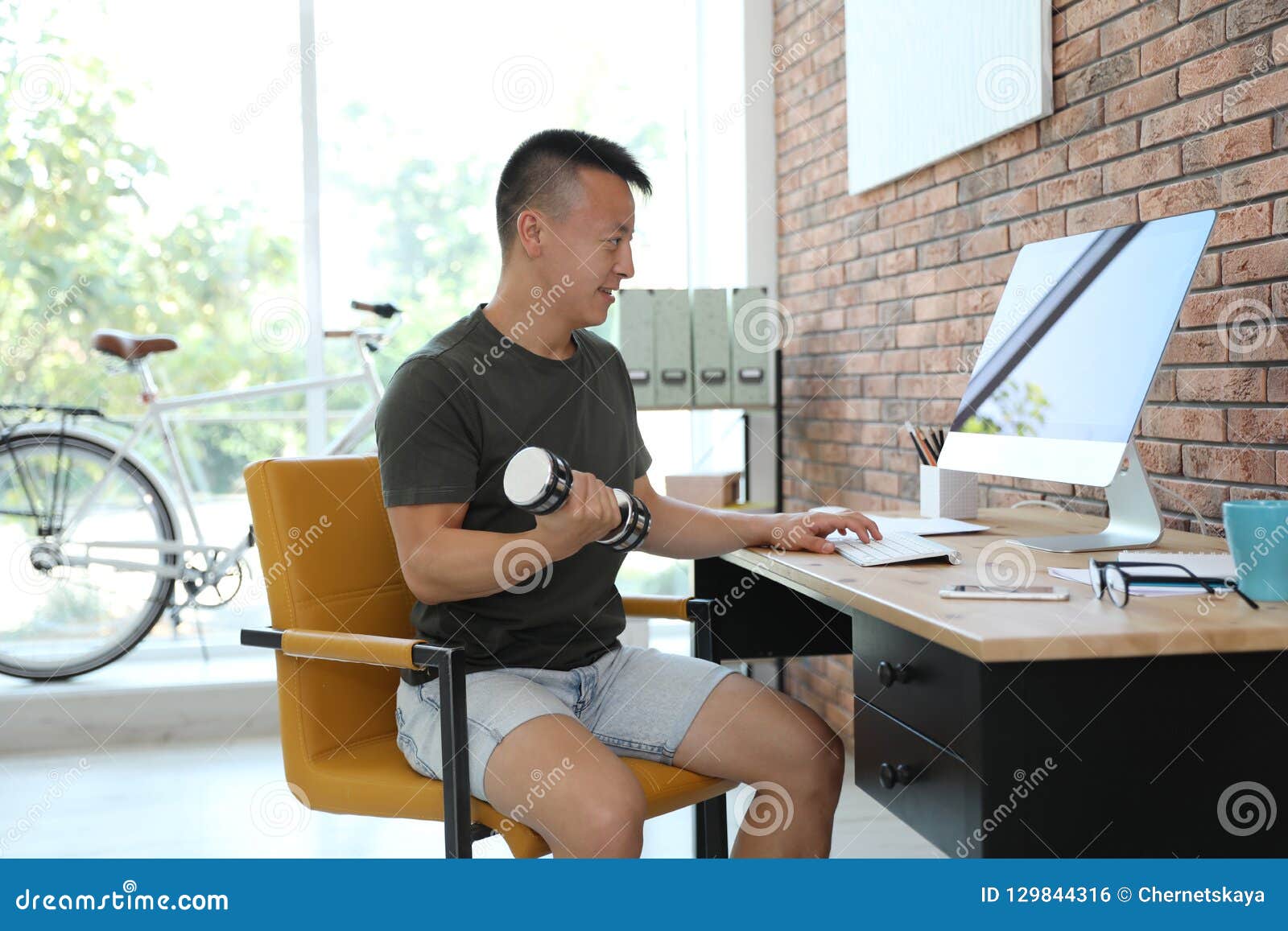 Young Man Lifting Weights and Using Computer in Office Stock Photo