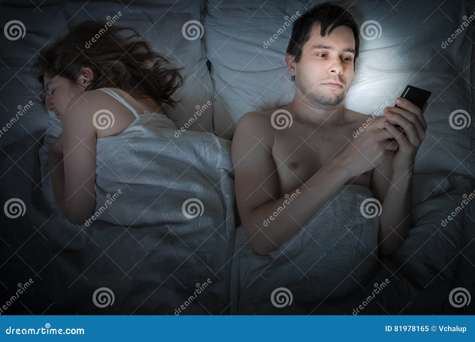 Young Man Is Lying With Girlfriend In Bed And Texting With Phone At