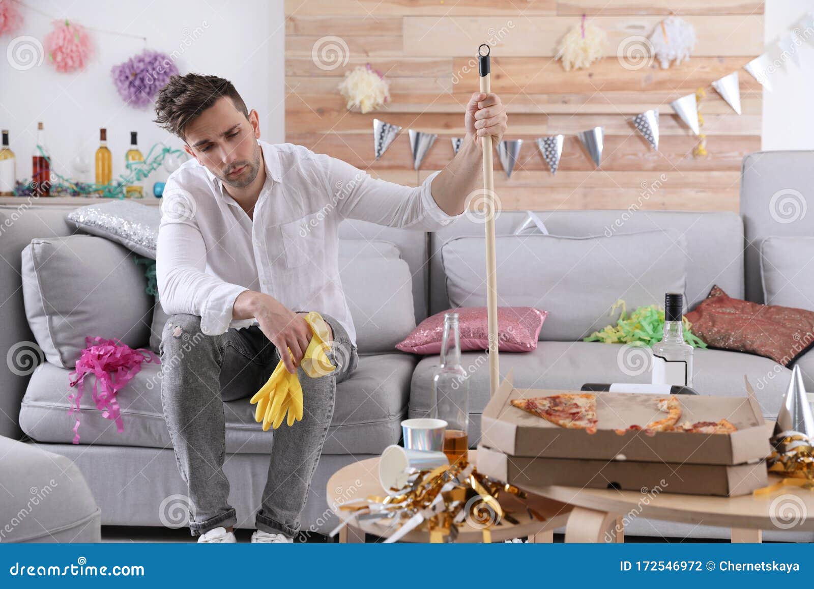 young man with mop suffering from hangover in room after party