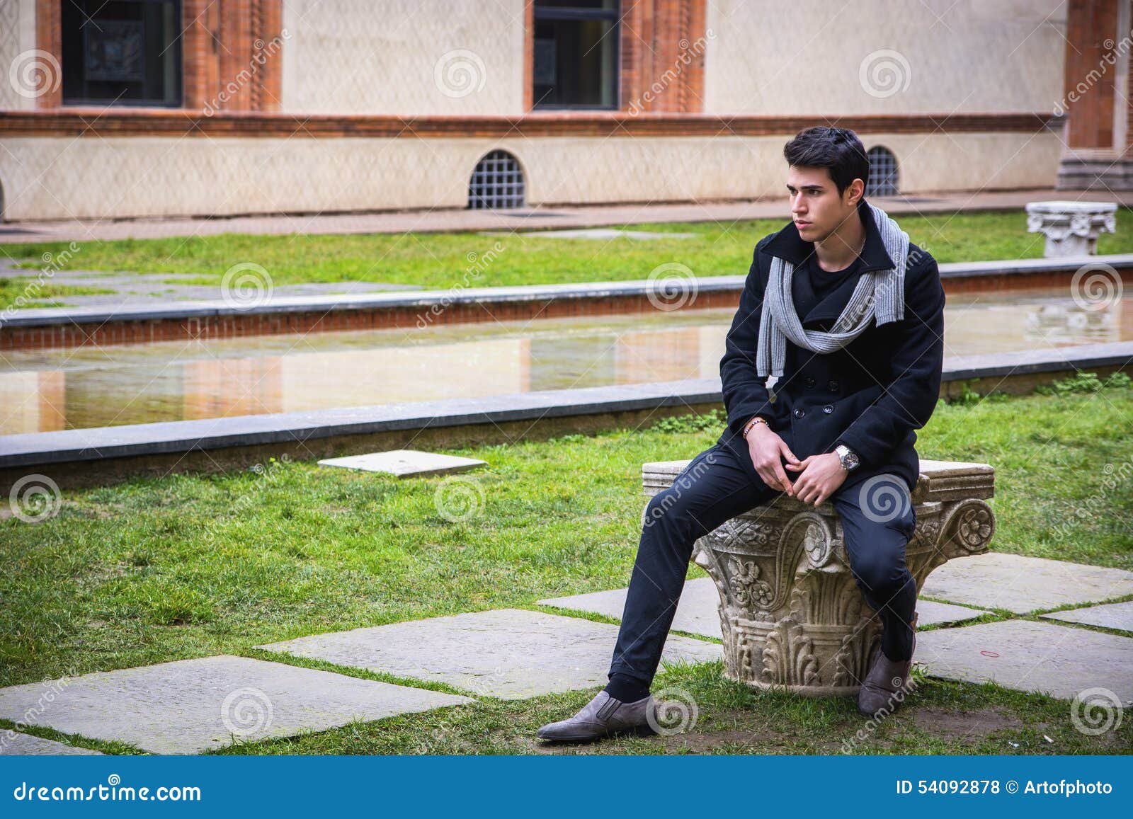 Young Man Outside the Building Looking Away to. Handsome Young Man Outside Ancient Castle or Building Looking Away to Left, Sitting on Stone
