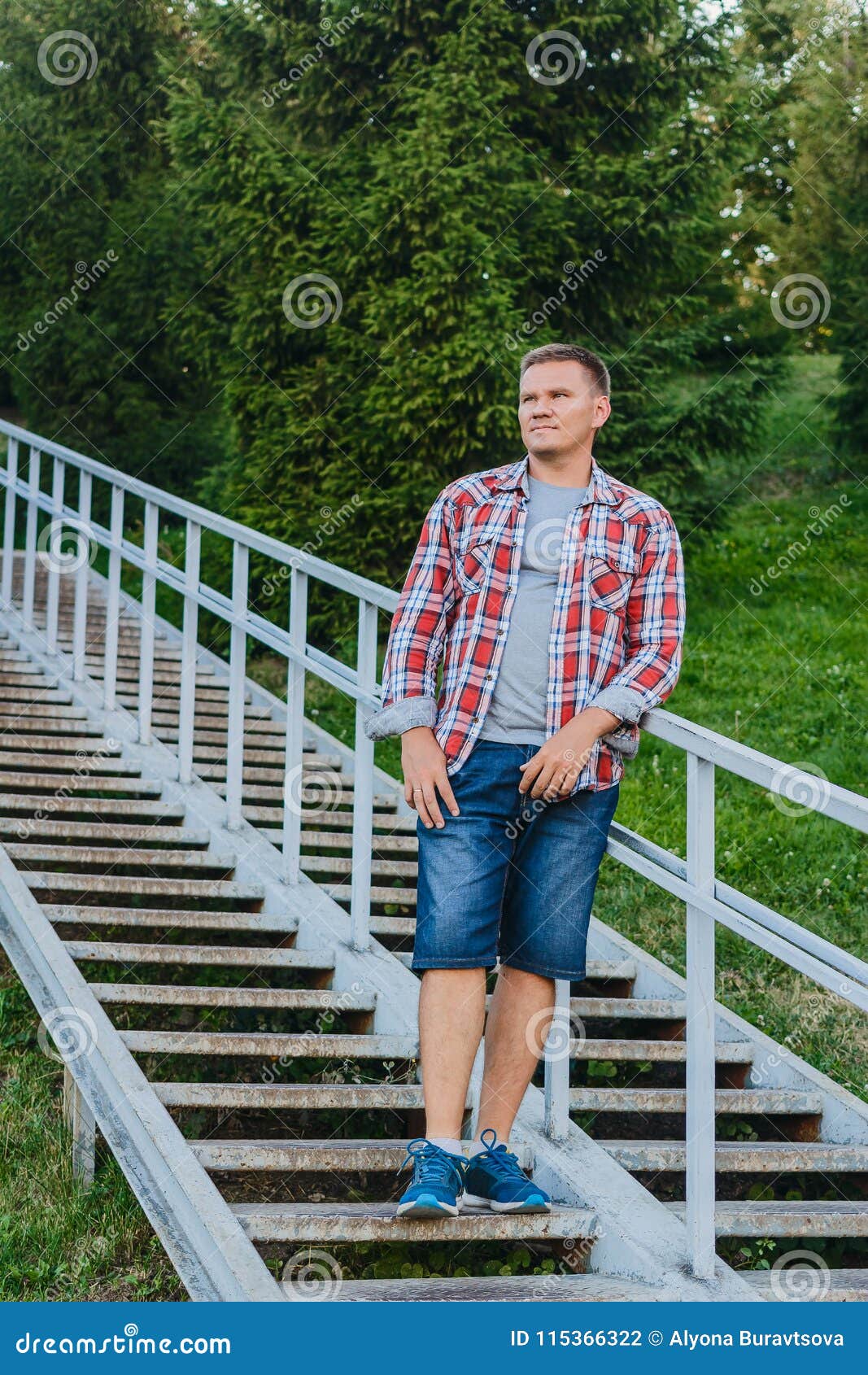 A Young Man in a Plaid Shirt and Denim Shorts Stands on a Metal Stock ...