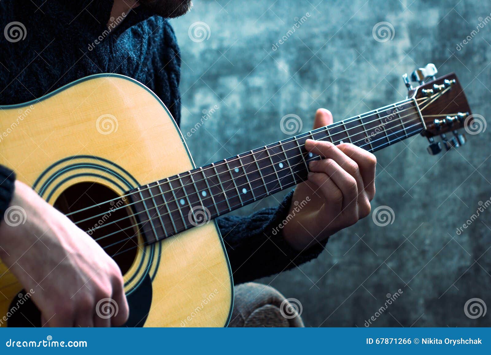 young man playing an acoustic guitar on the background of a concrete wall