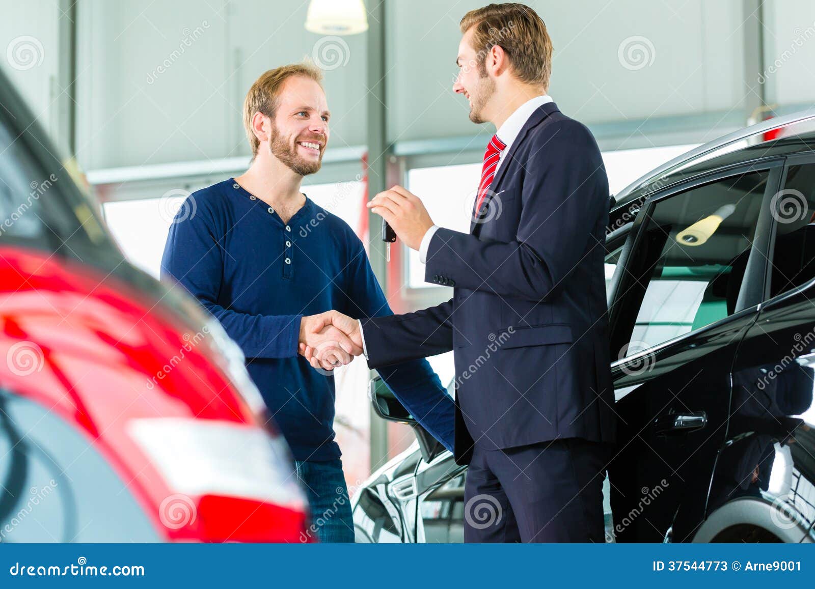 young man and seller with auto in car dealership