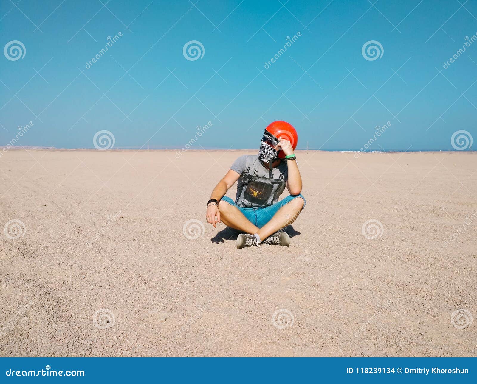 young man sits thoughtfully in the middle of desert wearing a helmet for buggy.