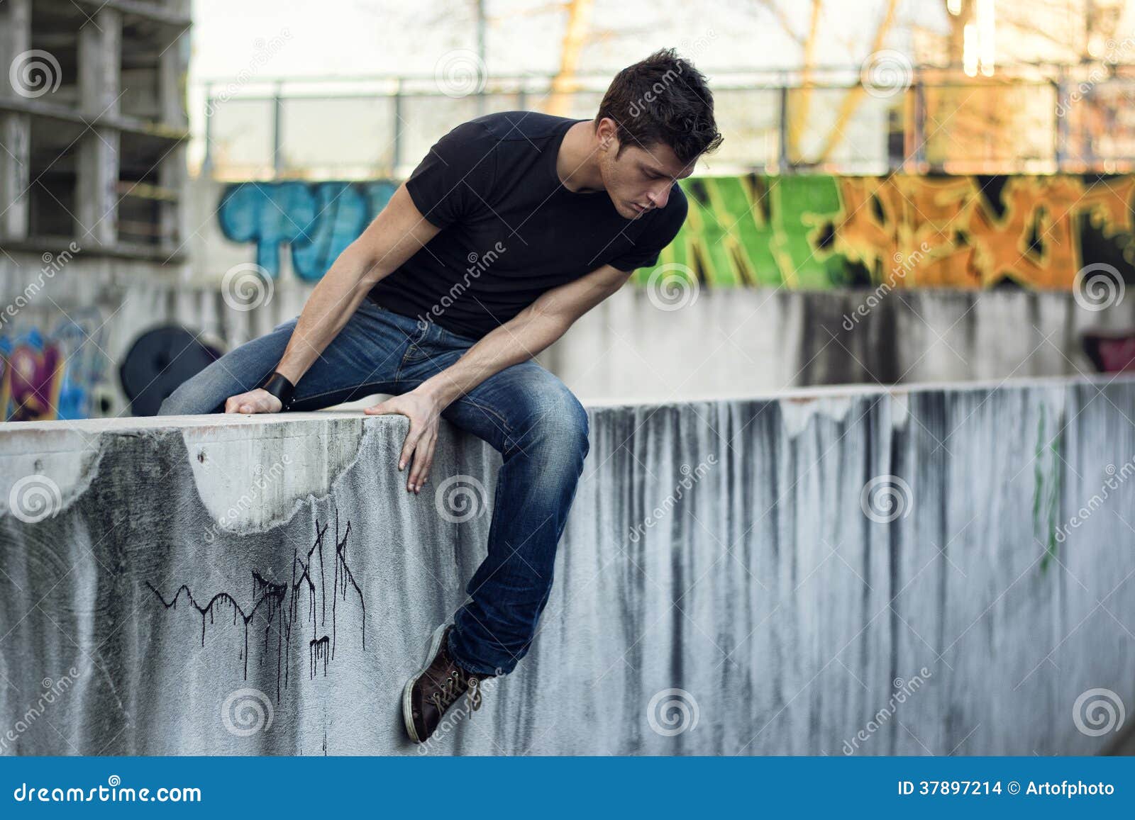 Young Man Sitting and Balancing on Wall, Looking Down Stock Photo